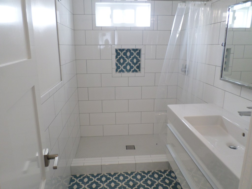 It looks like you've uploaded an image of a bathroom with a clean and modern design. The space has white subway tiles, an accent tile feature in the shower, and a vanity with a minimalist design. The accent tiles on the floor and in the shower niche provide a nice contrast to the white surroundings, adding character and color to the space.