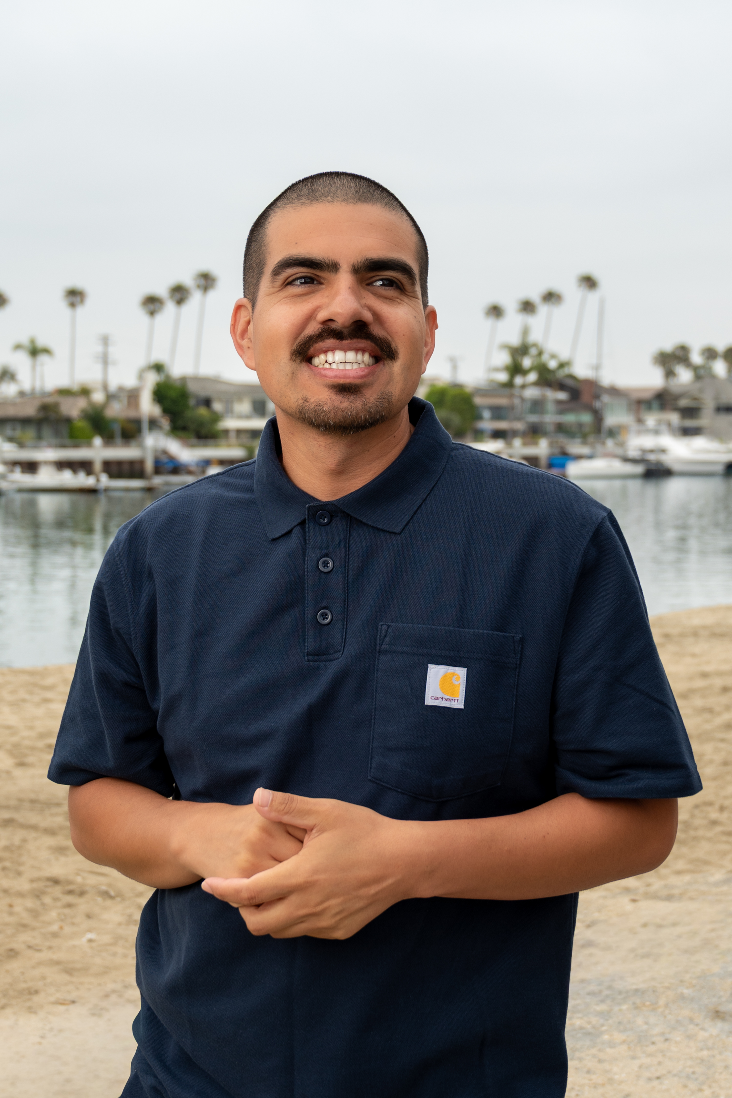 Enrique “Henry” Hernandez, owner of Handy Henry & Company, standing near the waterfront in Naples, Long Beach, wearing a navy work polo and smiling outdoors.